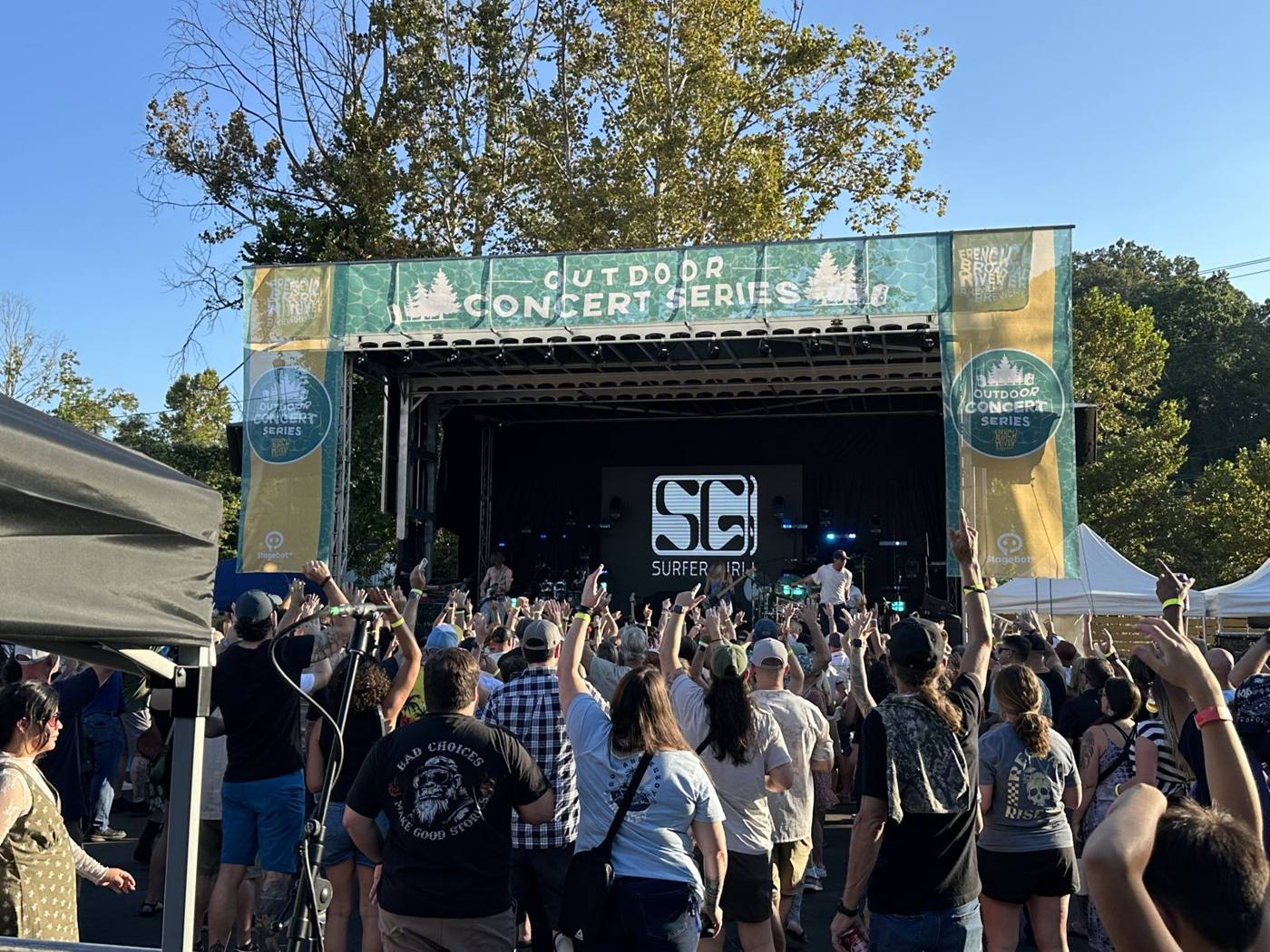 Daytime festival crowd with hands up at the Outdoor Concert Series